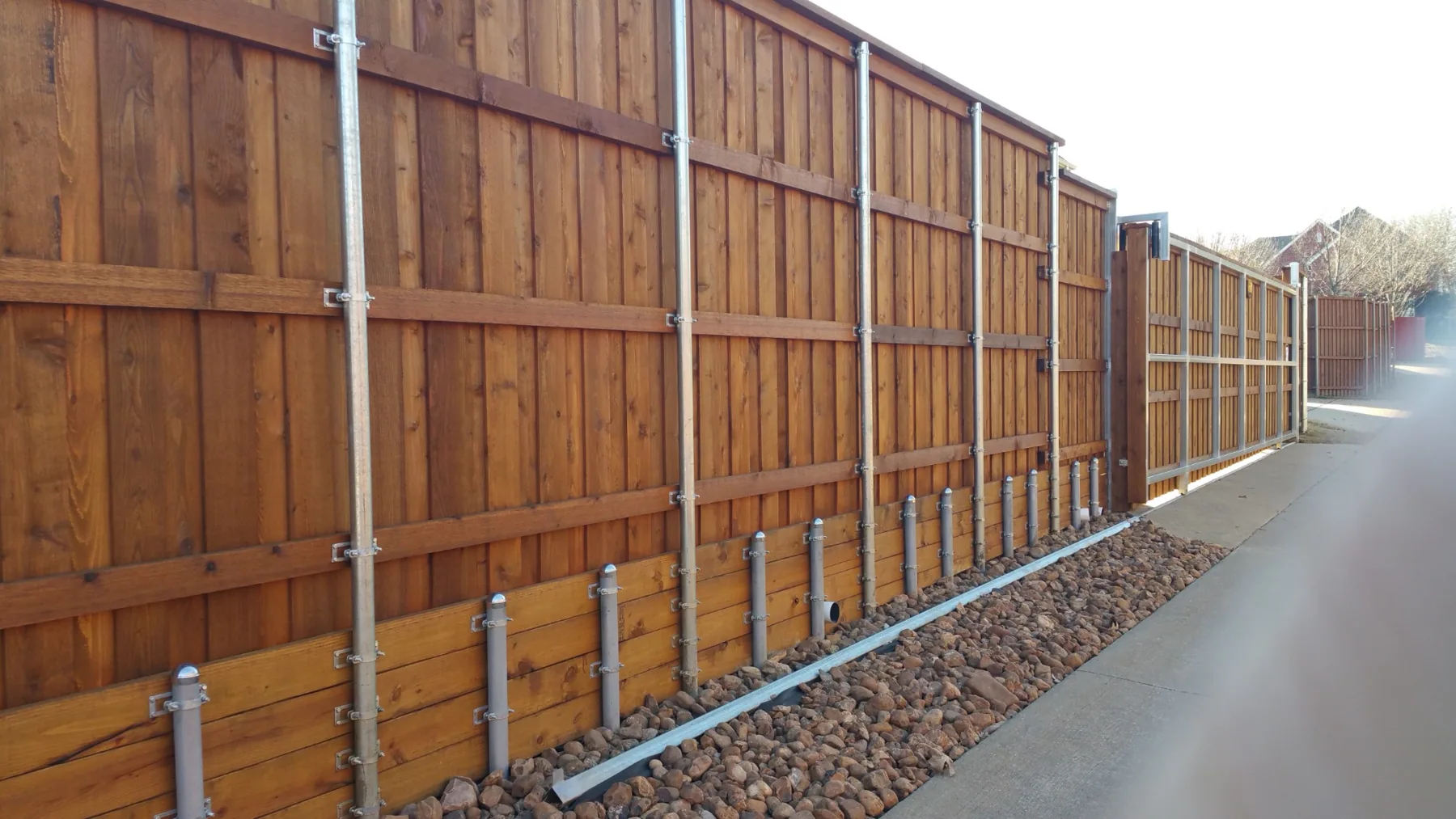 Long cedar fence with metal posts and a sliding gate